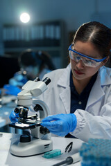 Asian female scientist wearing scientific glasses looking at a microscope Sample analysis, culture,...