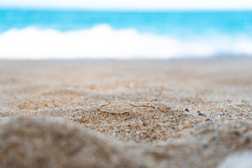 Close-up view of a sandy beach with a blurred turquoise sea in the background. The central part of the image is in focus, providing an ideal spot for placing objects or text in an editor. 