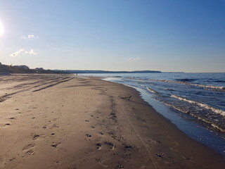 A peaceful sandy beach stretching along the coastline with gentle waves lapping the shore. The clear blue sky and distant horizon create a calm and relaxing seaside atmosphere, perfect for leisure.