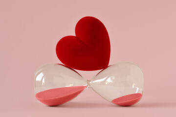 Heart on hourglass lying on pink background - Concept of time and love