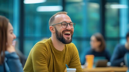 Obraz premium A man with glasses laughs joyfully in a bright, modern workspace, surrounded by others who seem engaged and happy.