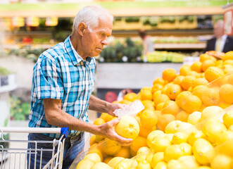 Mature senor examines oranges in fruit section of supermarket