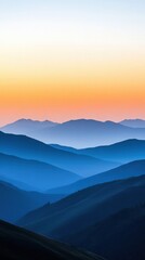 Fototapeta premium Layers of mountains stretch across the landscape during dawn, with soft blue tones gradually transitioning into warm orange shades in the sky. The serene atmosphere showcases natures beauty.