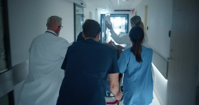 Diverse Emergency Medical Team Rushing Down a Hospital Corridor, Carefully Pushing a Stretcher with an Injured Patient. Nurses and Doctors Coordinate the Urgent Situation. Follow Footage