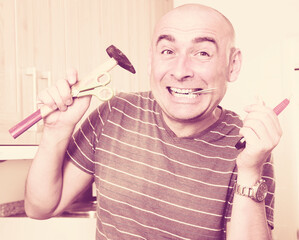 imposing man in prime of life holds in teeth of screws and holding hammer