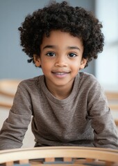 Fototapeta premium A young boy with curly hair is smiling and wearing a brown sweater