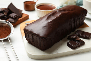 Tasty sponge cake, pieces of chocolate and cocoa powder on white table, closeup