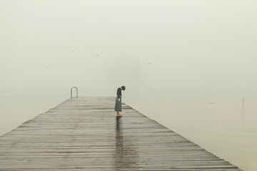 lonely woman with her head down on a pier overlooking the winter sea