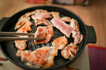 Hand of Using stainless steel chopsticks, there is grilled sliced ​​pork or MOO KA TA, grilled food on a pan, Asian style eating.