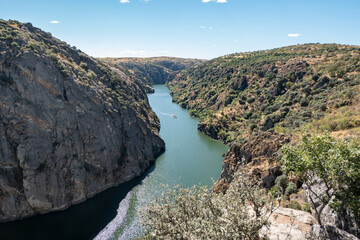 Em meio a paisagem natural com montanhas, vegetação e um céu azul, o rio Douro em Miranda do Douro com um pequeno barco ao fundo em Portugal © LuIvDa