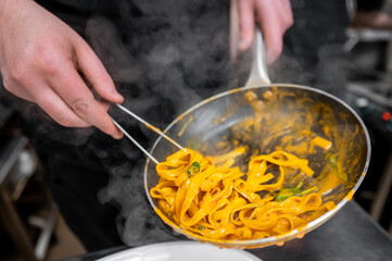 close-up of hands cooking pasta with vegetables in a steaming pan. The vibrant colors of the...