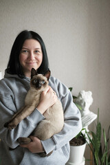 Young woman holding a blue-eyed Siamese cat. Cat and its owner at home. Caring for pets. Selective focus.