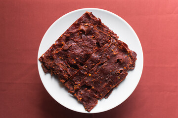 Overhead view of Nigerian kilishi on a white plate, top view of nigerian spicy beef jerky, flatlay of dried beef suya