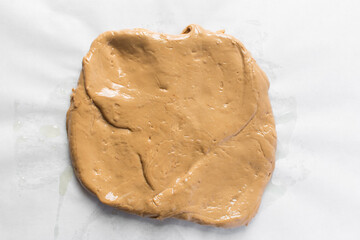 Overhead view of iloka candy on parchment paper, top view of cooked condensed milk candy shaped into a log, Nigerian iloka candy on a white background, process of making caramel hard candy