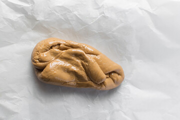 Overhead view of iloka candy on parchment paper, top view of cooked condensed milk candy shaped into a log, Nigerian iloka candy on a white background, process of making caramel hard candy