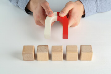 Man with magnet attracting wooden cubes at white table, closeup