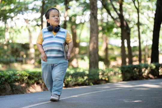 Confident Asian woman with dwarfism walking in park with headphones