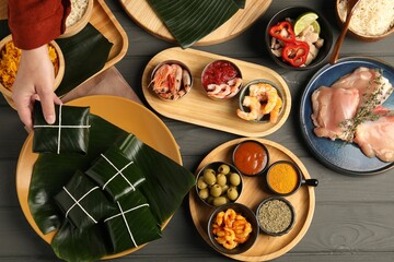 Woman taking folded banana leaf with food at wooden table with products, top view