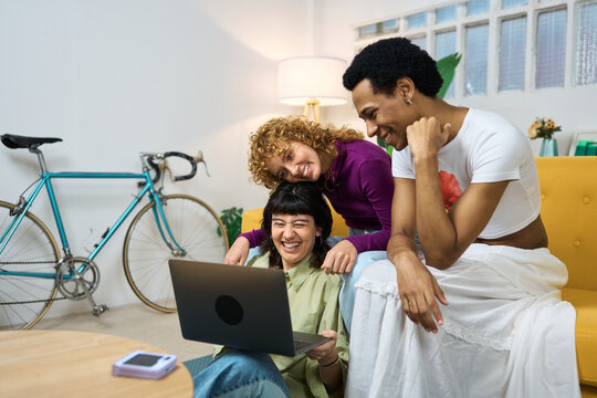 Happy lgtb friends laughing and watching a laptop at home
