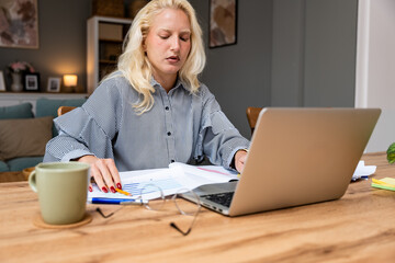 Businesswoman working on laptop computer sitting at home and managing her business via home office...