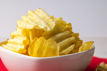 Potato chips in white bowl, on red napkin, with white background. Appetizer and snack.