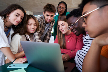 Multiracial group of students gathered in the university, sitting on a table studying together and doing homework using a laptop. Copy space image.