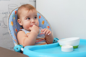 Adorable baby sitting in a high chair with a playful expression and finger sucking