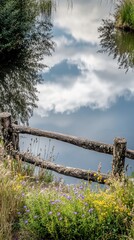 Fototapeta premium A serene pond scene with a wooden fence and vibrant wildflowers reflecting in the water.