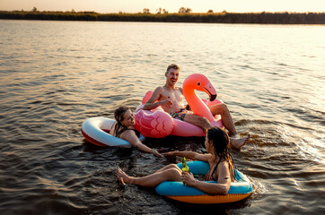 Group of friends having fun and enjoying a summer day swimming with rubber tube and drinking beer at the lake.