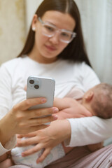 Beautiful young woman wearing white clothes is breastfeeding her baby at home, close-up back view. She is working only at the same time, remote work from home