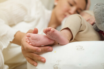 The palms of the mother are holding the foot of the newborn asian baby. Close-up family photo of a child's toes, heels and feet.
