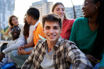 Cheerful portrait of a young caucasian male student looking at camera while sitting outside university gathering with friends.