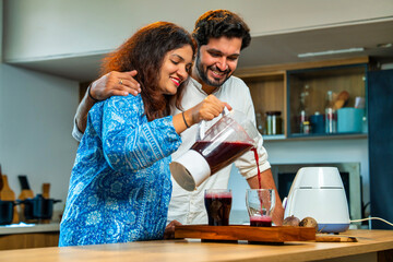 Indian wife serves fresh red beetroot juice to her husband in the kitchen, promoting healthy living
