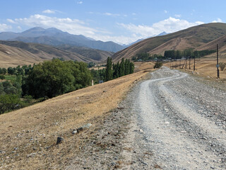 View of landcape with mountains and hills. Beautiful clouds above mountains. Dirt road on a...