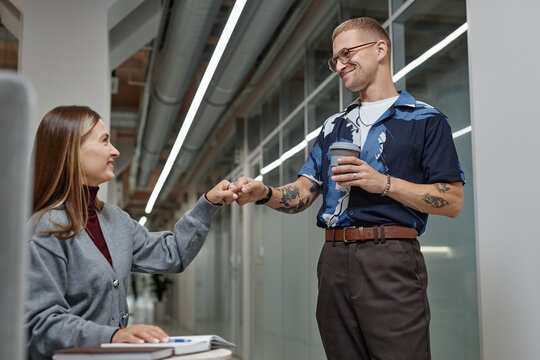 Side view of positive male businessman fist bumping with female coworker rejoicing at project success while collaborating in common area of modern office building, copy space