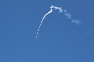 Smoke trail of a flying signal rocket against clear blue sky, bright red light at the tip, detailed curve, isolated view, dynamic motion, minimalistic composition