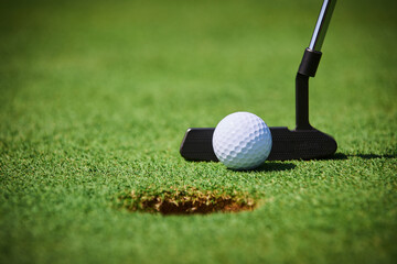 White golf ball near a hole with a black putter on a green field, close-up view, clear focus, professional golfing equipment, outdoor sports concept