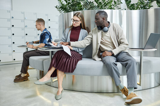 Full length shot of African American businessman consulting with female colleague about document, while working collaboratively in lounge area of modern coworking space with light minimalistic design - Powered by Adobe