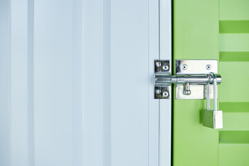 Background image of metal latch with lock on green door leading to self storage unit at warehouse,...