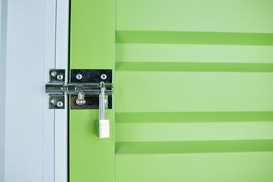 Background shot of green door leading to self storage unit with metal latch secured on lock at warehouse, copy space
