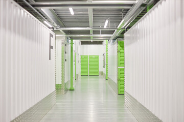 Background image of passway with white walls and green metal doors leading to self storage units at...