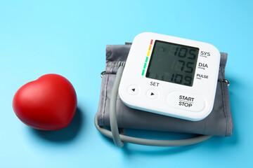 Blood pressure measuring device and red heart figure on light blue background