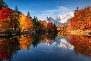 Tranquil lake surrounded by autumn trees and mountains, with vibrant red, orange, and yellow leaves mirrored on the water's surface, ai.