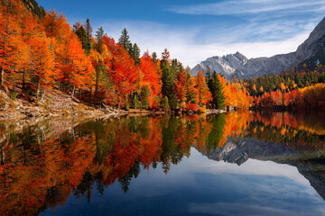 A serene lake reflects colorful autumn trees and mountains, with bright red, orange, and yellow foliage creating a picturesque scene, ai.