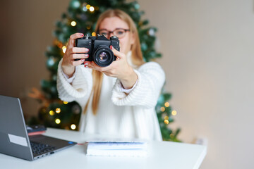 Naklejka premium girl holding a camera against the background of a Christmas tree. Copy space