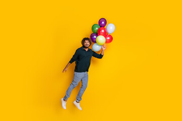 Young man in black shirt with colorful balloons floating against yellow background, conveying sense of fun, joy, celebration.