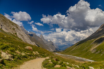 Val Veny scenic landscape in Courmayeur valley, Italy on Tour du Mont Blanc hiking route. Alps beautiful landscape, scenic view of the alpine peaks, green fields and meadow with flowers and blue sky