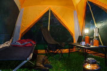 Camping tent, folding bed inside the tent at night in the forest, gas lantern and coffee set,...
