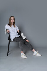 A girl sits with one arm resting on a chair, looking straight ahead. This portrait captures the...