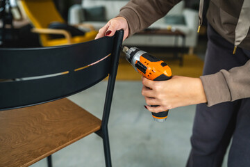 close up of woman use electric screwdriver on black metal chair